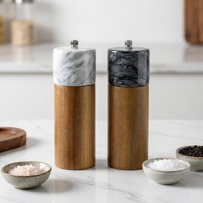 White and black marble-topped acacia wood salt and pepper mills beside small bowls of salt and peppercorns on a marble counter