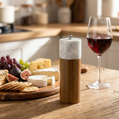 White marble-topped acacia wood mill beside a cheese board with grapes and figs and a glass of red wine