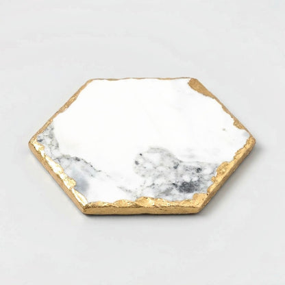 Large hexagonal white marble coaster with grey marbling and gold edging on an off-white background