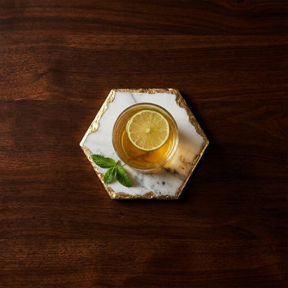 Overhead view of a hexagonal white marble coaster with gold edging holding a glass of tea with a lime slice on a dark wood table