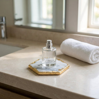 Glass perfume bottle on a hexagonal white marble coaster with gold edging on a stone bathroom vanity