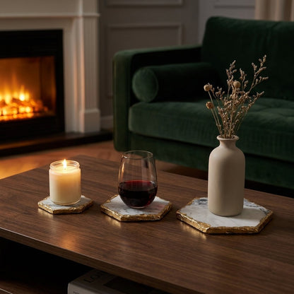 Three hexagonal marble coasters with gold edging holding a candle, a glass of red wine and a vase of dried flowers on a coffee table in front of a fireplace