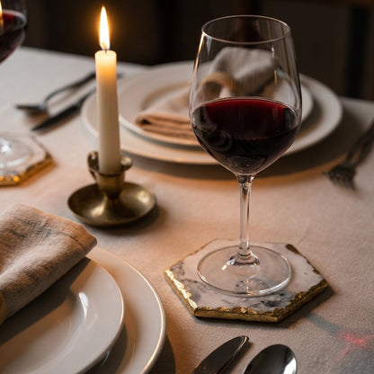 Hexagonal white marble coaster with gold edging under a glass of red wine on a candlelit linen dinner table