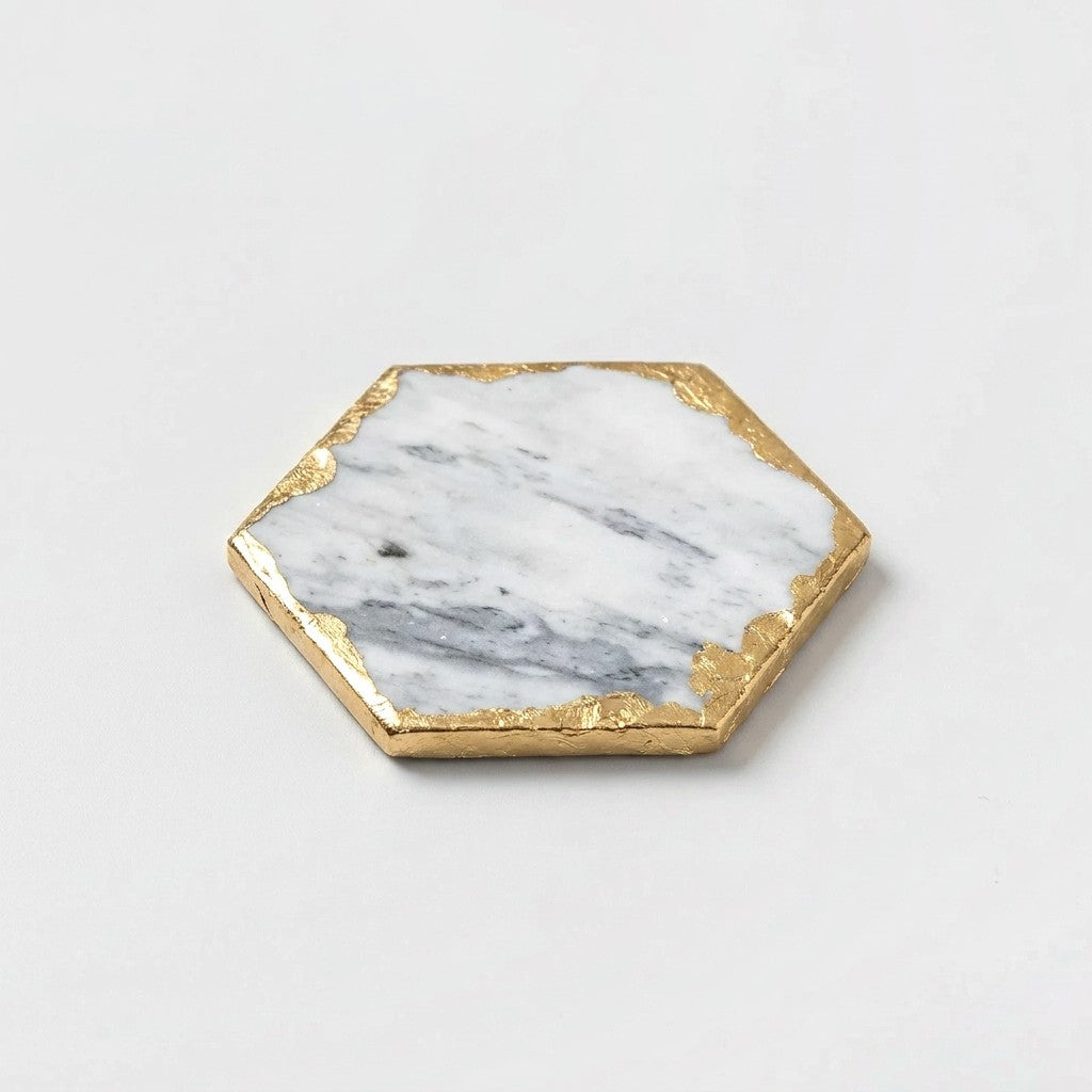 Small hexagonal white marble coaster with grey veining and gold edging on an off-white background