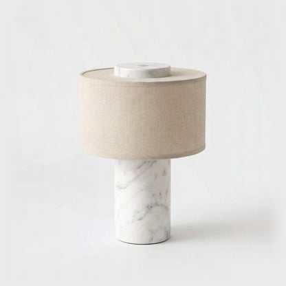 Portable table lamp with a white marble base and soft grey veining and a natural linen drum shade on a plain light backdrop
