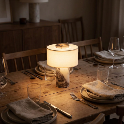 Dining table set with plates, glasses, and cutlery under a warm lamp in a cozy room.