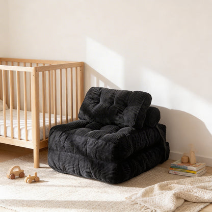 Black plush chair in a room with a wooden crib and toys on a light-colored floor.