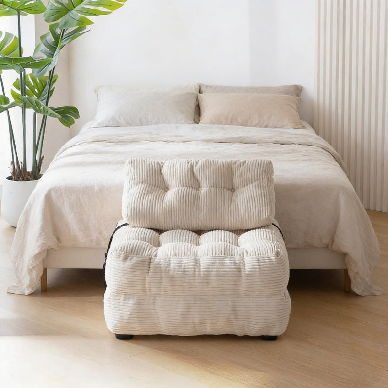 Beige ottoman with tufted design in front of a bed in a bedroom setting