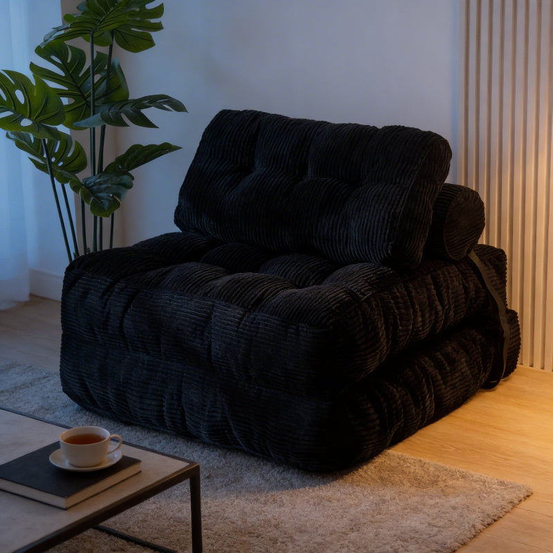 Black textured armchair in a room with a plant and a small table with a cup.