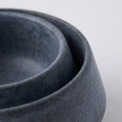 Close-up of two nested speckled slate-blue stoneware bowls with soft rounded rims on a light grey background