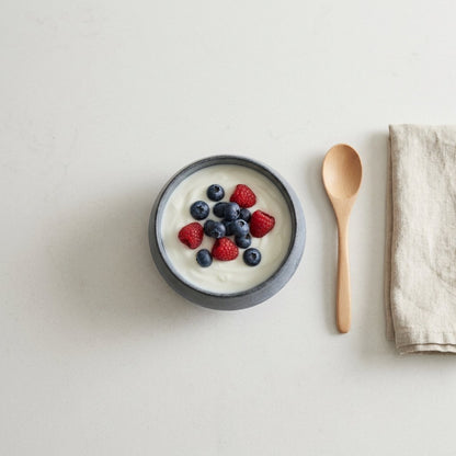 Overhead view of a small speckled blue stoneware bowl of yogurt with blueberries and raspberries on a pale stone surface
