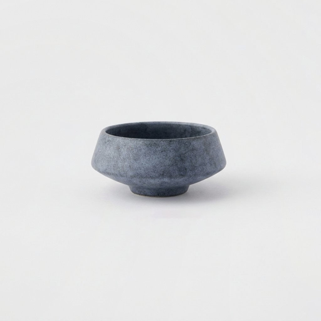 Small matte speckled blue stoneware bowl on a light grey background