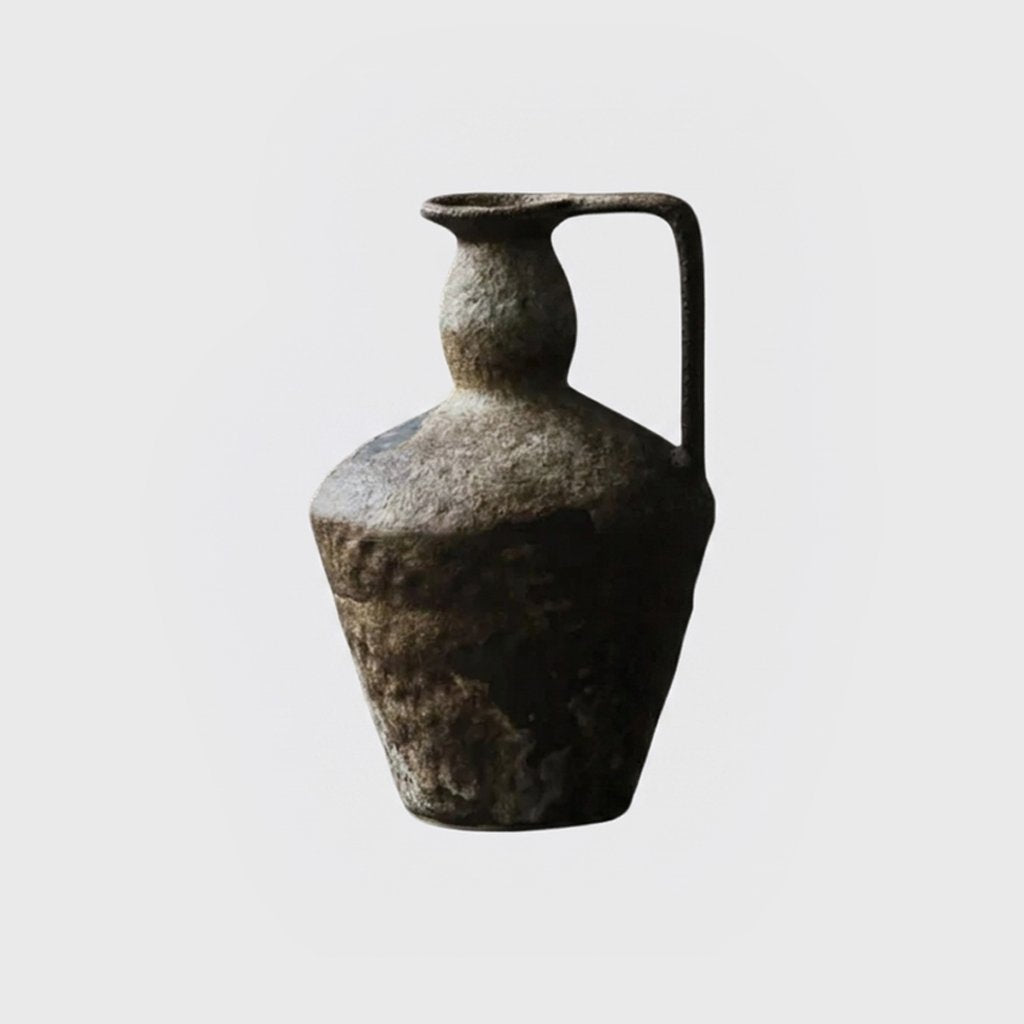 Single empty dark brown-gray rough-textured ceramic pitcher vase with a narrow neck and one strap handle on a plain light gray background