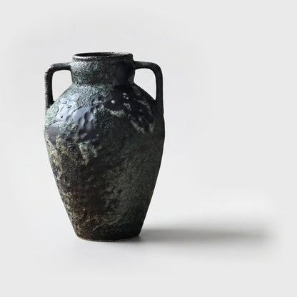 Single empty dark forest green two-handled ceramic amphora vase with a glossy black patch on the shoulder on a plain light gray background