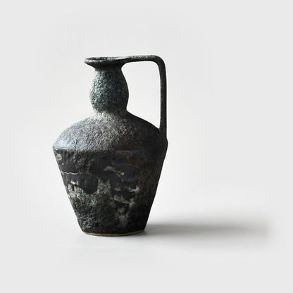 Single empty dark charcoal green-gray ceramic pitcher vase with a glossy black glaze band and one strap handle on a plain light gray background