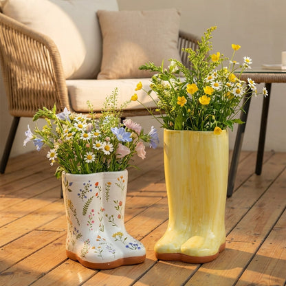 Two rain boots repurposed as planters with flowers on a wooden deck.