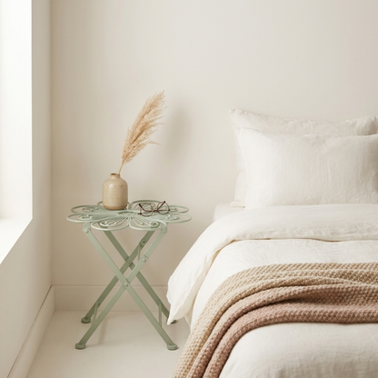 Metal flower bistro table beside bed in bright neutral bedroom