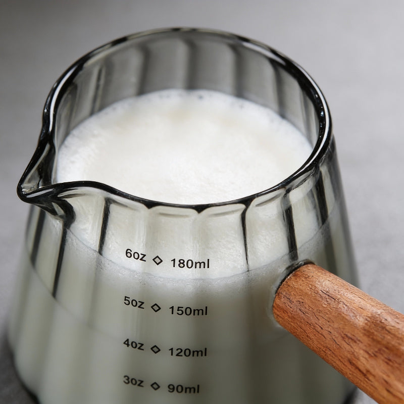 Glass measuring cup with wooden handle filled with milk, close-up on a neutral background