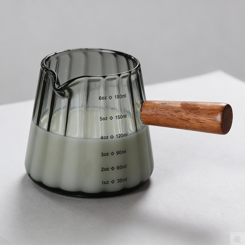 Glass measuring cup with wooden handle on a white surface