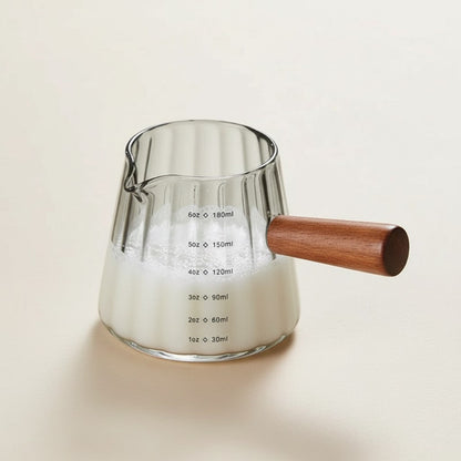 Glass measuring cup with wooden handle on a light background