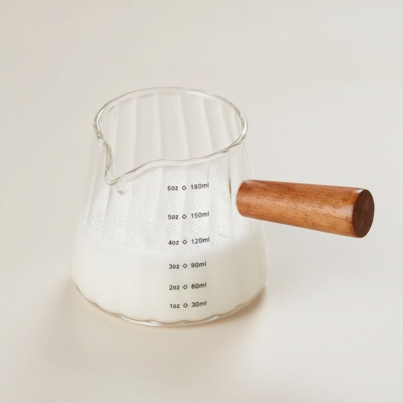 Clear glass measuring cup with wooden handle on a light background