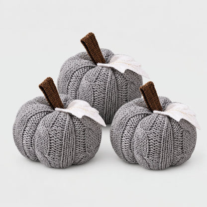 Set of three grey cable-knit mini pumpkins with brown stems and white felt leaves on a plain light backdrop