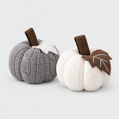 Grey and cream mini knit pumpkins side by side with brown stems and felt leaves on a plain light backdrop