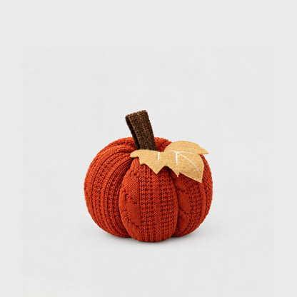 Single rust orange mini knit pumpkin with a brown stem and tan felt leaf on a plain light backdrop