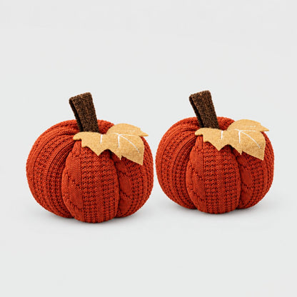 Two rust orange mini knit pumpkins side by side with brown stems and tan felt leaves on a plain light backdrop