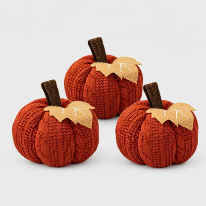 Set of three rust orange mini knit pumpkins with brown stems and tan felt leaves on a plain light backdrop