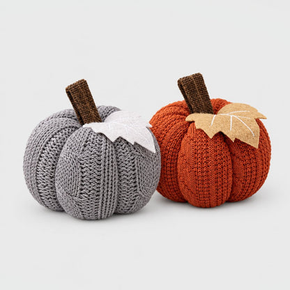 Grey and rust orange mini knit pumpkins side by side with brown stems and felt leaves on a plain light backdrop