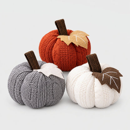 Set of three mini knit pumpkins in rust orange, grey and cream with brown stems and felt leaves on a plain light backdrop