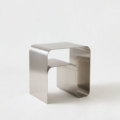 Empty brushed stainless steel arch side table with a flat top and a lower half-depth shelf on a plain light backdrop