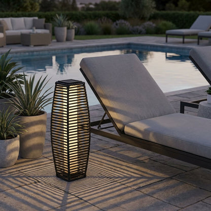 Lit outdoor solar floor lantern beside a pool on a stone patio with lounge furniture and potted agave plants
