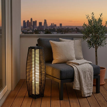 Lit outdoor solar floor lantern on a rooftop balcony at sunset with a city skyline in the background
