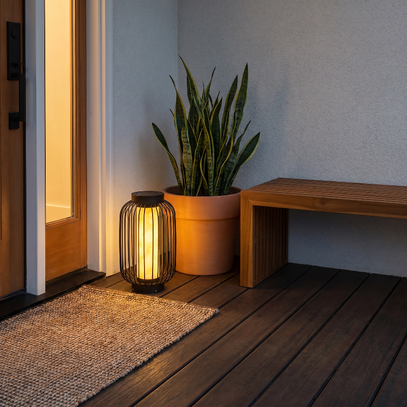 Modern outdoor solar lantern on deck beside potted plant at dusk