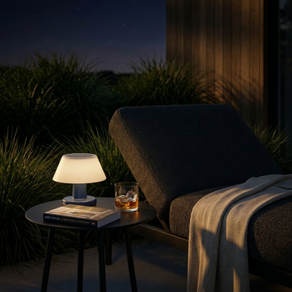 Modern portable solar table lamp on outdoor side table beside lounge chair at dusk