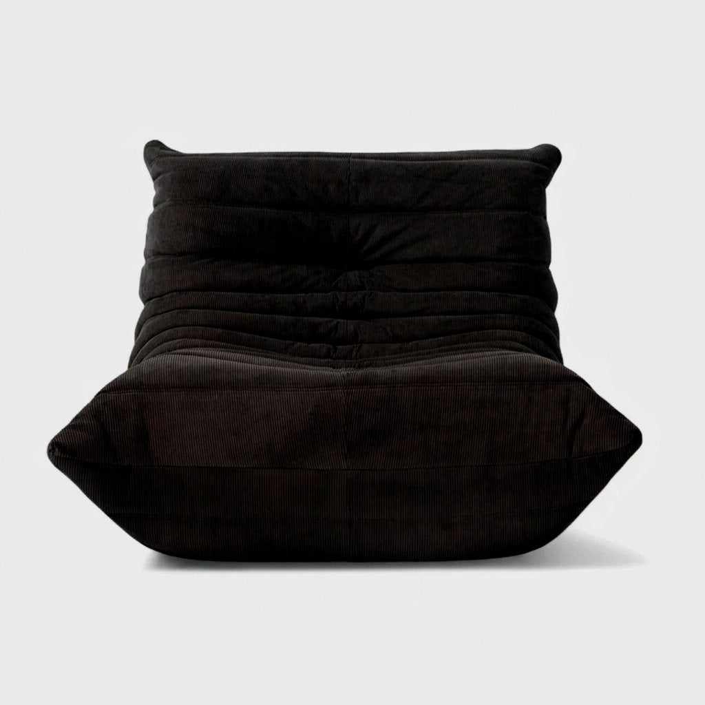 Black corduroy tufted lounge chair seen from the front on a light studio background