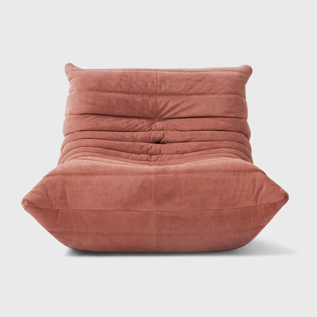 Dusty pink corduroy tufted lounge chair seen from the front on a light studio background