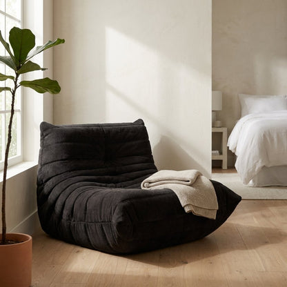 Black corduroy tufted lounge chair with a knit throw in a bedroom with a potted fiddle-leaf fig