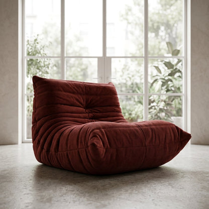 Maroon corduroy tufted lounge chair in front of white-framed glass patio doors with greenery outside