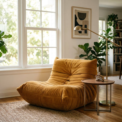 Mustard corduroy tufted lounge chair beside a brass arc floor lamp, walnut side table, and bookshelf