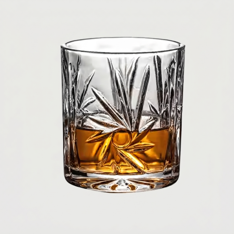 Decorative glass with etched design filled with amber liquid on a light gray background