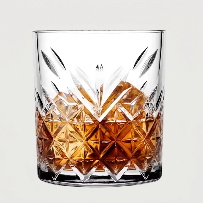 Clear glass with diamond-cut design filled with amber liquid on a light gray background