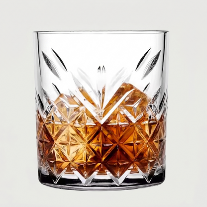 Clear glass with diamond-cut design filled with amber liquid on a light gray background