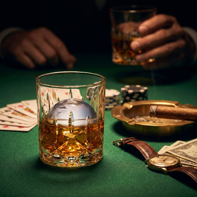 Glass of whiskey on a green table with playing cards, chips, and a cigar.