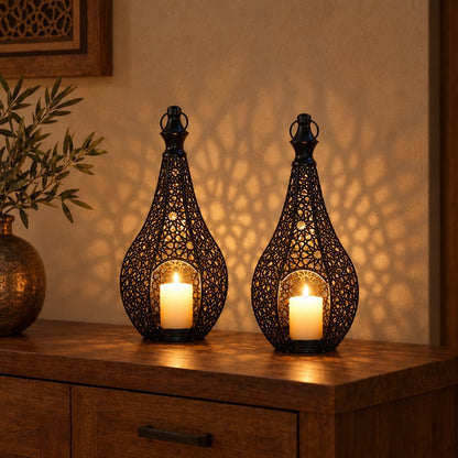 Two black cutwork metal lanterns with lit pillar candles on a wood sideboard, casting patterned shadows on the wall