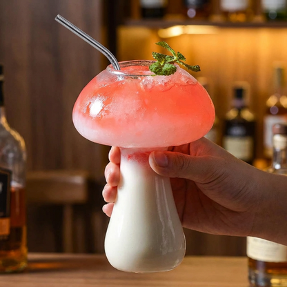 Mushroom-shaped cocktail with pink liquid and a straw, held by a hand in a bar setting.