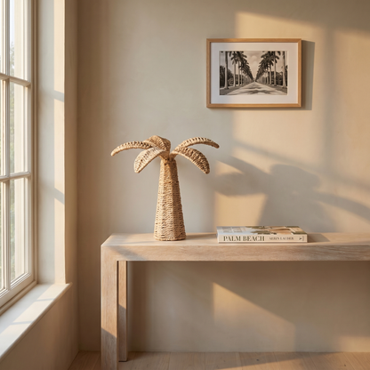 Decorative palm tree sculpture on a wooden table with a framed picture of a palm tree in the background.