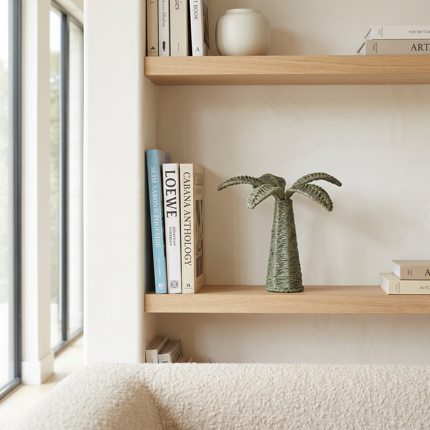 Wooden shelves with books and a decorative palm tree sculpture against a light wall.